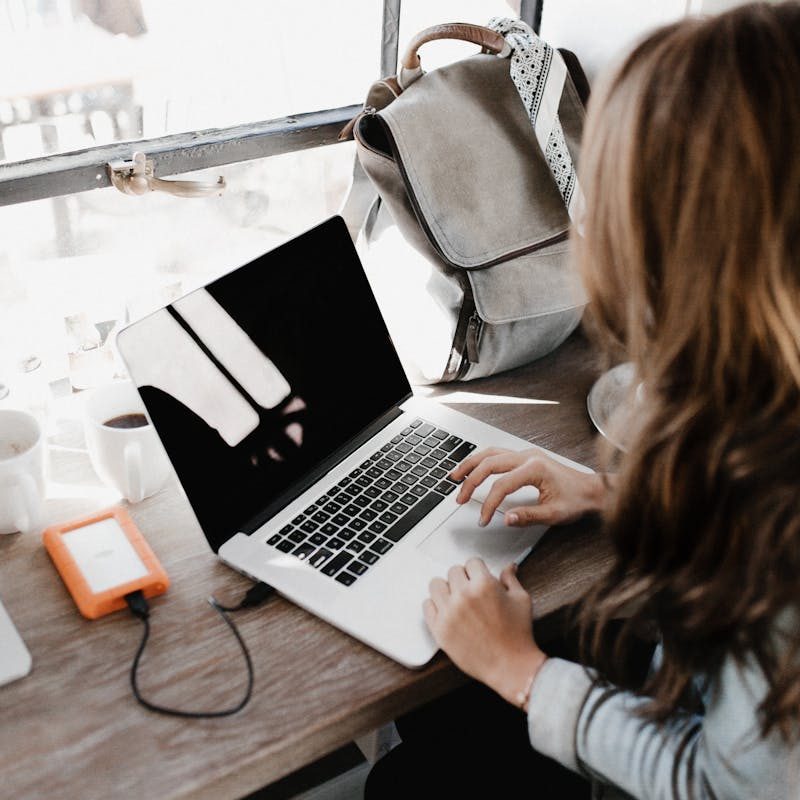 Close-up Photography of Woman Sitting Beside Table While Using Macbook